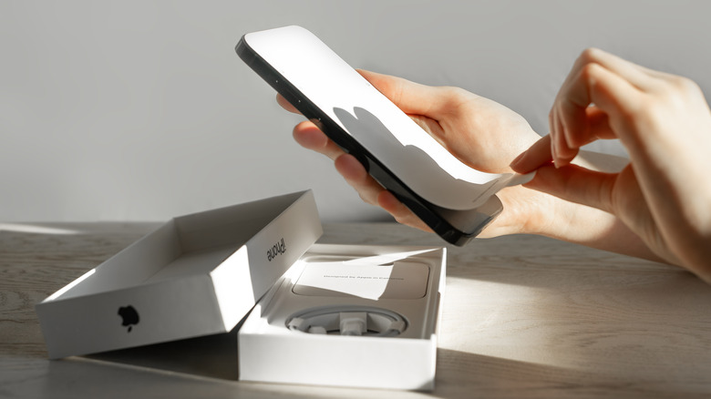 Person inspecting a smartphone and removing its protective film beside an opened box, illustrating how to check an open-box product’s condition and included accessories.